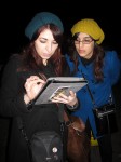 Vanessa Crooks (left), 27, and Carolina Sato, 23, try to locate their friend via iPad using a marathon app that helps track runners. Crooks and Sato, whose friend still hadn't appeared at the finish line by 8 PM Sunday night, are both from Panama. Photo by Louie Lazar.