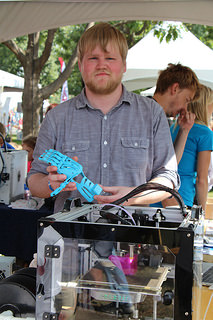 A 3D printer is making a prosthetic hand made of thin plastic, similar to the blue one Ryan Brandy holds. Plastic prosthetics are more affordable than bio-prosthetic limbs. Photo by Maria Panskaya